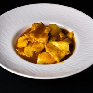 Close-up of a delicious chicken curry dish beautifully plated in a white ceramic bowl on a dark background.