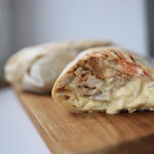 Tasty chicken wrap filled with creamy sauce on a wooden cutting board.