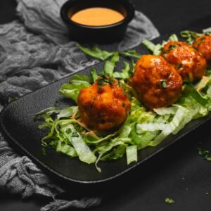 Close-up of spicy meatballs served on fresh lettuce with a dipping sauce. Perfect for food photography enthusiasts.