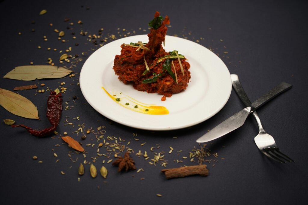 A deliciously arranged spicy Indian chicken dish garnished with herbs, surrounded by aromatic spices on a dark background.