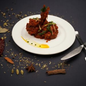 A deliciously arranged spicy Indian chicken dish garnished with herbs, surrounded by aromatic spices on a dark background.