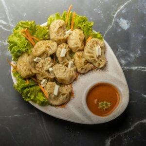 Tasty homemade paneer momos served with spicy chutney on a marble background.