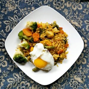 Delicious vegetable fried rice topped with a sunny side up egg, served on a white plate.