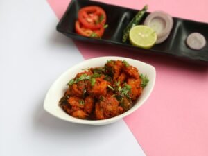 Delicious spicy chicken fry garnished with cilantro and served with fresh vegetables on a pink background.