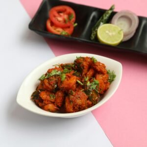 Delicious spicy chicken fry garnished with cilantro and served with fresh vegetables on a pink background.