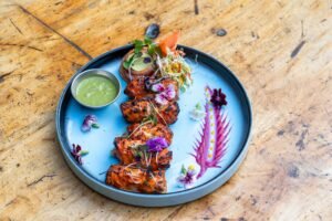 A beautifully plated grilled tandoori chicken dish with vibrant floral garnishes, ideal for food lovers.