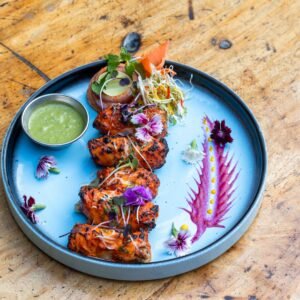 A beautifully plated grilled tandoori chicken dish with vibrant floral garnishes, ideal for food lovers.
