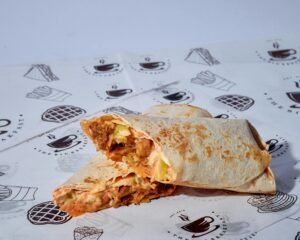 Close-up of a grilled chicken burrito with vegetables, sliced diagonally on a decorative paper wrap.