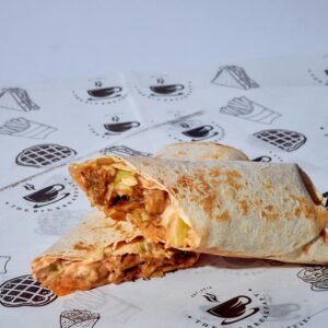 Close-up of a grilled chicken burrito with vegetables, sliced diagonally on a decorative paper wrap.