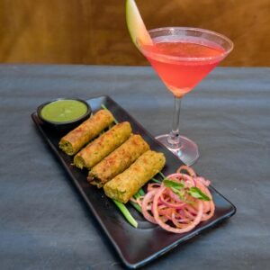 From above of yummy deep fried Vietnamese spring rolls on plate with onion slices and spicy green salsa near glass of cocktail in cafeteria