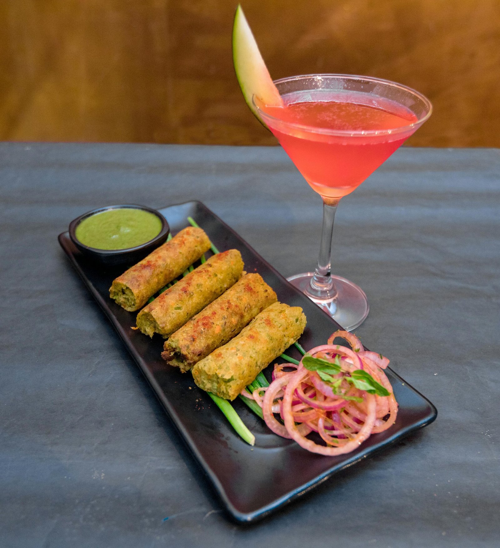 pexels-photo-4105288-4105288 From above of yummy deep fried Vietnamese spring rolls on plate with onion slices and spicy green salsa near glass of cocktail in cafeteria