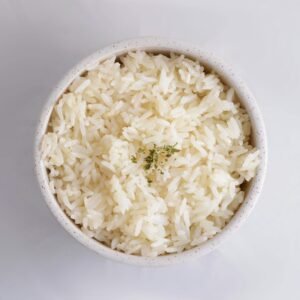 Close-up of cooked white rice in a bowl, garnished with herbs, in a minimalist setup.