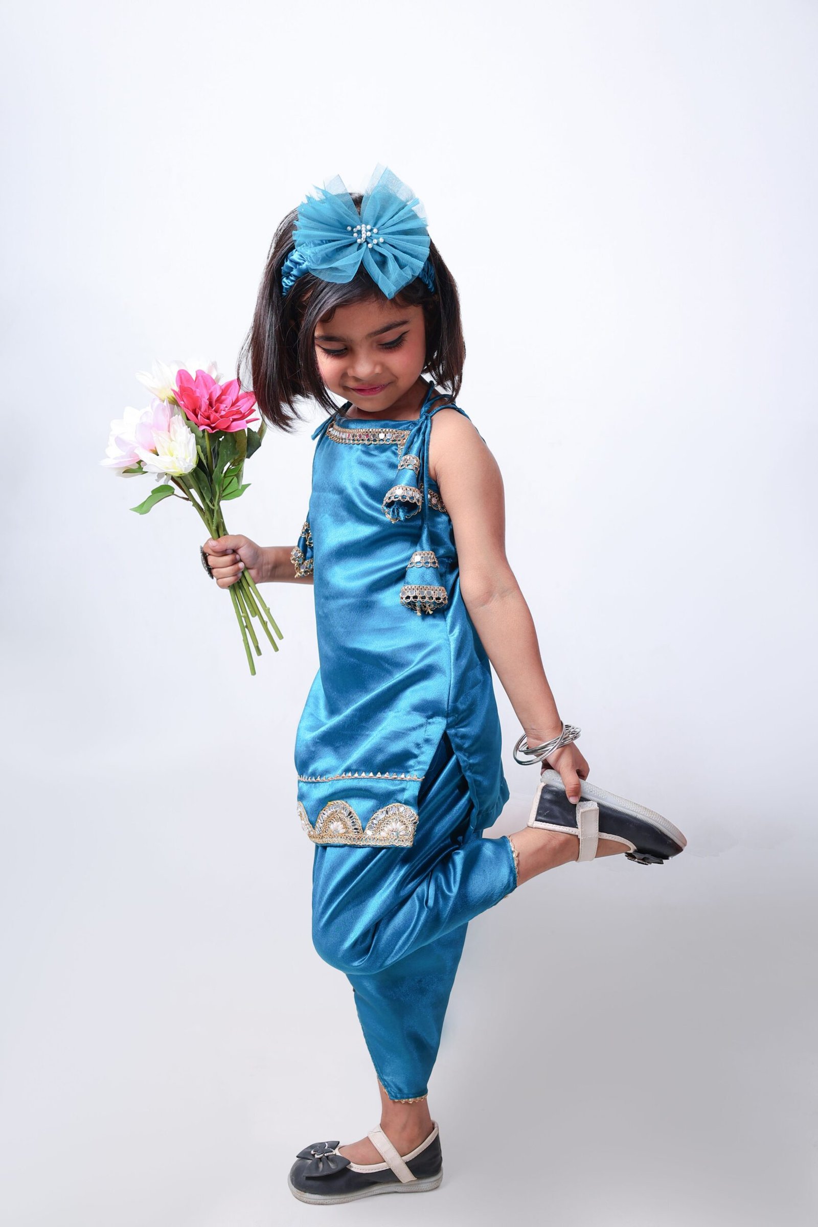 Adorable young girl in traditional blue attire holding a bouquet of pink and white flowers.